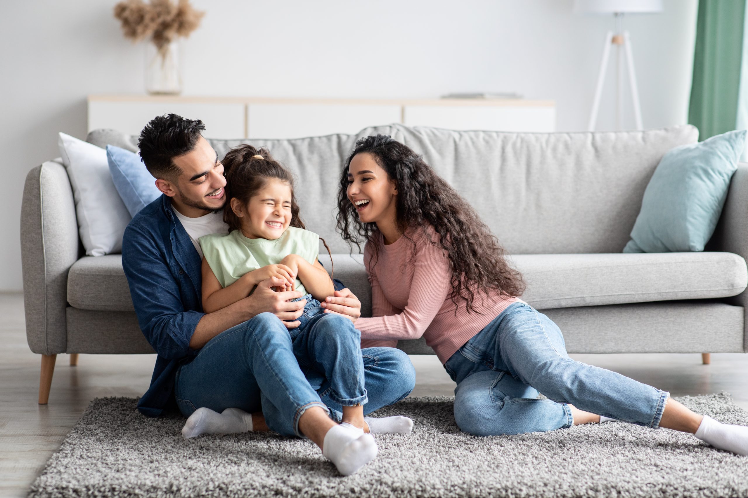 Man, woman and daughter are sitting in front of a couch